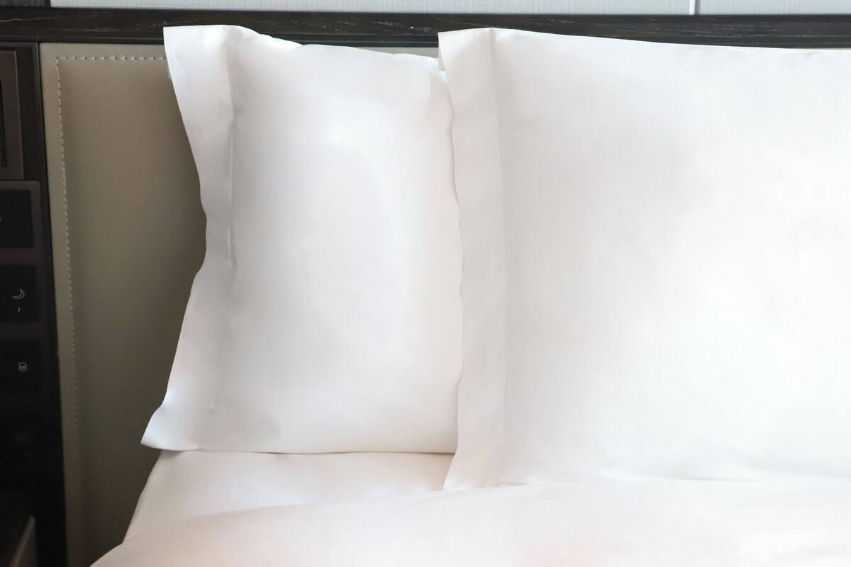 A neatly made bed with white linens and pillows.