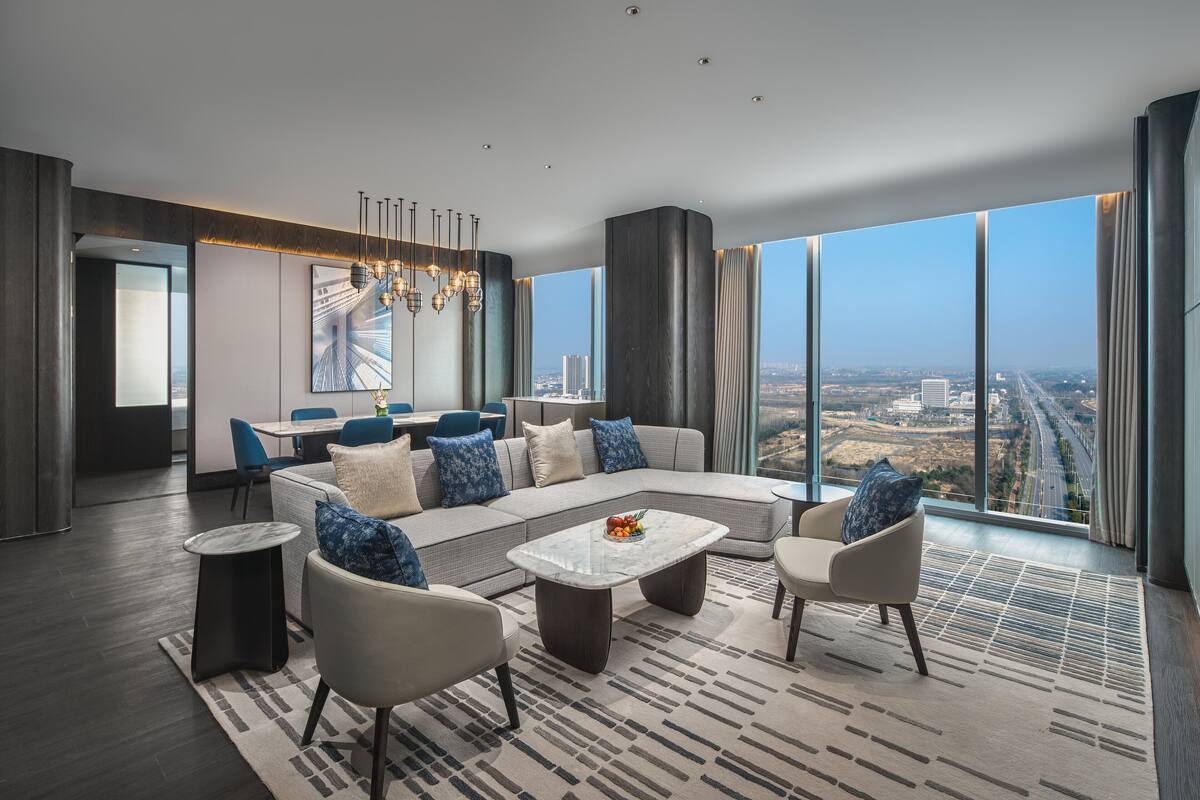 A modern living room with a sectional sofa, a coffee table, and a view of a cityscape through large windows.