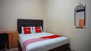 A neatly made bed with a patterned bedspread and two red pillows, a wooden nightstand, and a mirror on the wall.