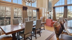 Un vaste espace dédié à la salle à manger, avec une grande table et des chaises en bois, un lustre et une vue sur l’extérieur grâce à de grandes fenêtres.