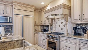Une cuisine avec des meubles de couleur beige, des plans de travail en granit, une cuisinière en acier inoxydable et un four à micro-ondes.