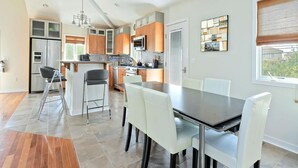 A modern kitchen with a dining area, featuring a central island, white chairs, and a large window. - 6 BR, Pool, Hot Tub and 5 min to Ocean (Loveladies)