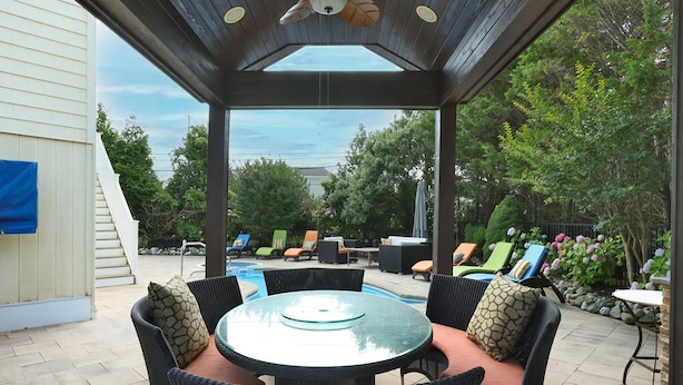 A covered patio with a round table and chairs, a ceiling fan, and a view of a swimming pool and trees. - 6 BR, Pool, Hot Tub and 5 min to Ocean (Loveladies)