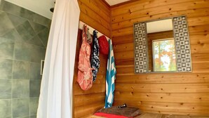 Bany d'una cabana de fusta amb dutxa, un mirall amb marc decoratiu i una panxa amb una tovallola vermella.