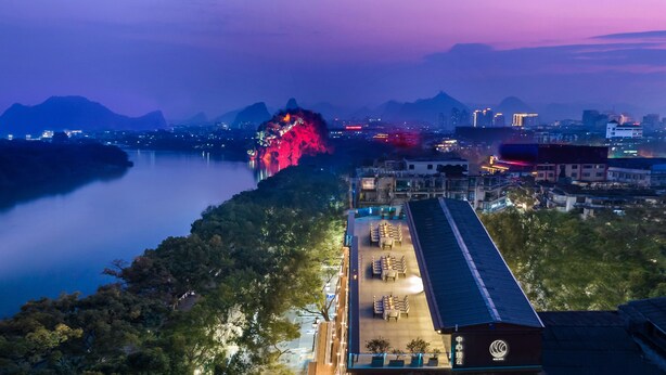 A hotel with a dining area and a view of a river and mountains.