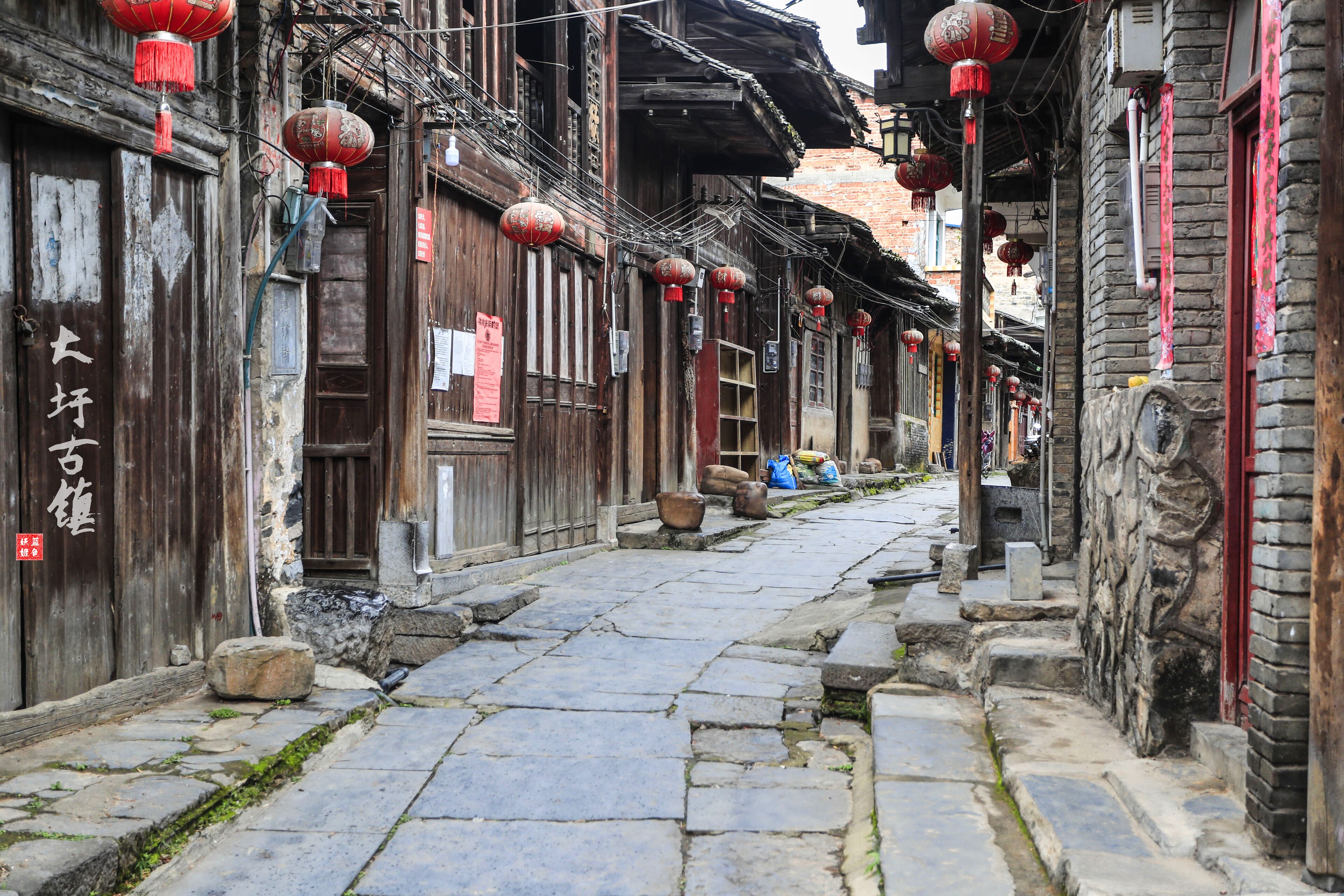 Una calle estrecha con edificios tradicionales de madera, adoquinado de piedra y faroles rojos.