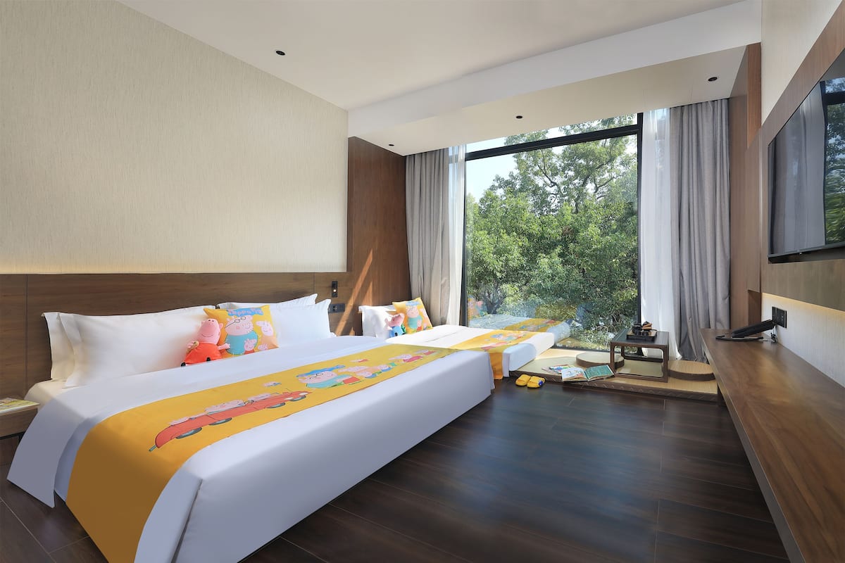 A hotel room with a large bed, a smaller bed, a desk, and a large window with curtains.