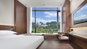 A modern hotel room with a large bed, a desk, and a view of a mountainous landscape.