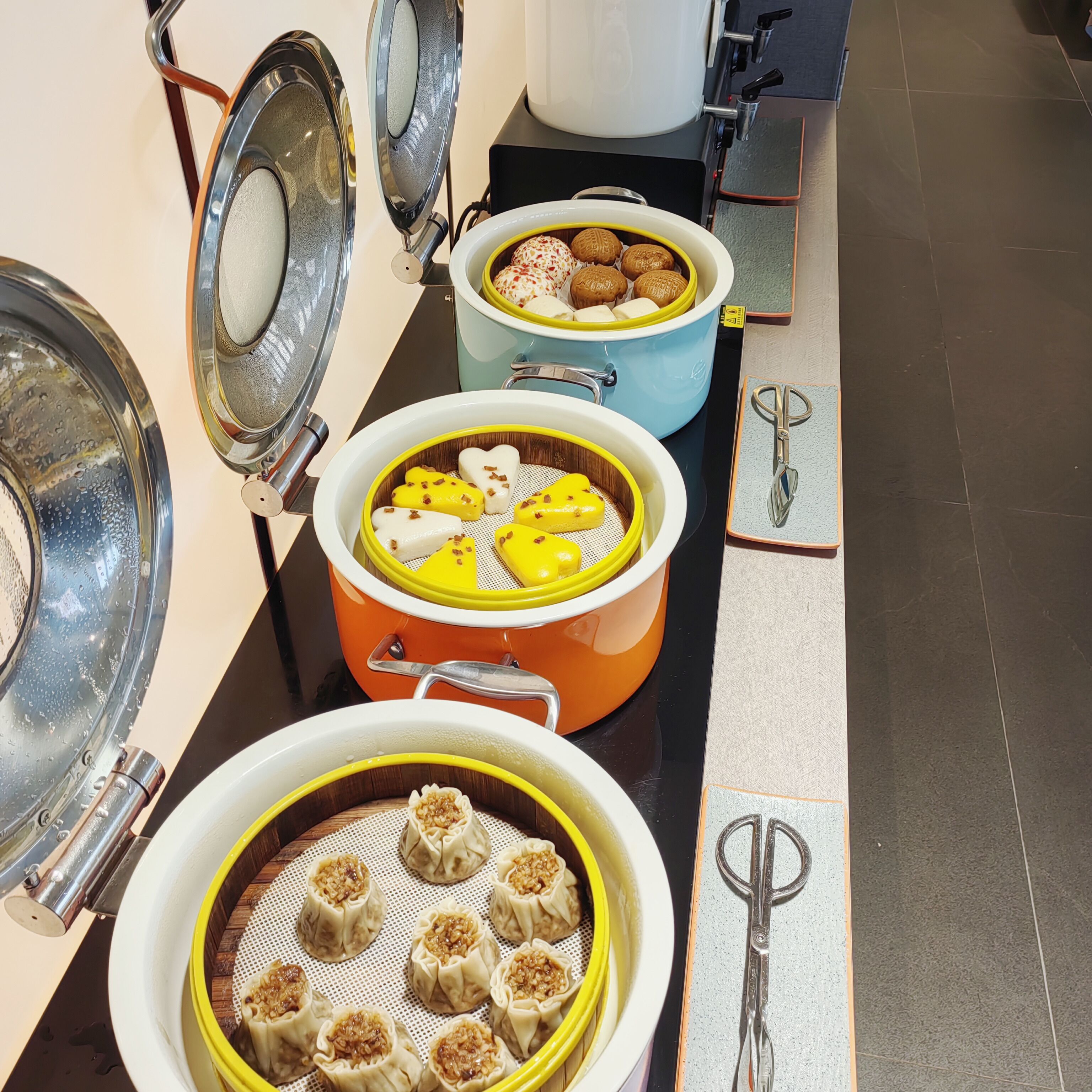 A buffet setup with various dishes in pots and a pair of scissors on the table.