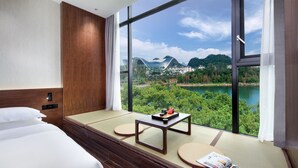 Habitación de hotel con un ventanal grande, una cama, una mesita y una revista en el asiento junto a la ventana.