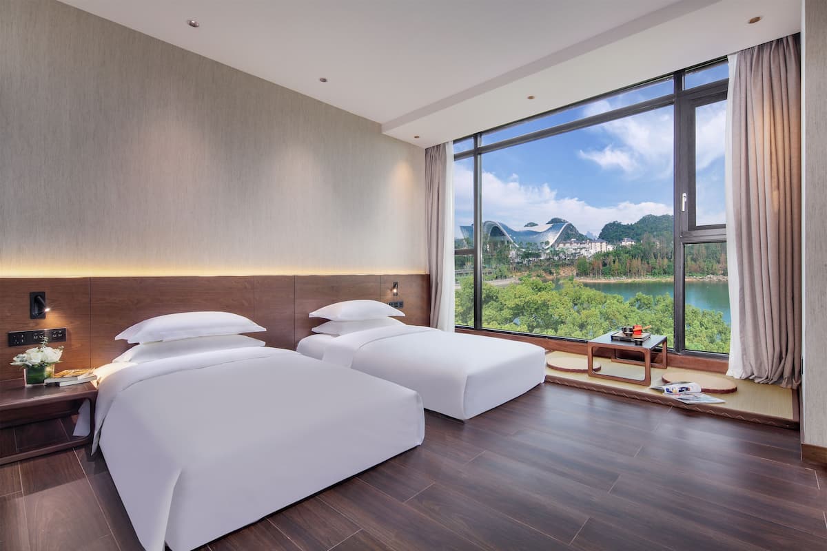 A hotel room with two beds, a nightstand, and a view of a lake and mountains.