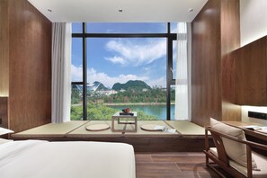 A modern hotel room with a large window offering a scenic view of mountains and a lake.