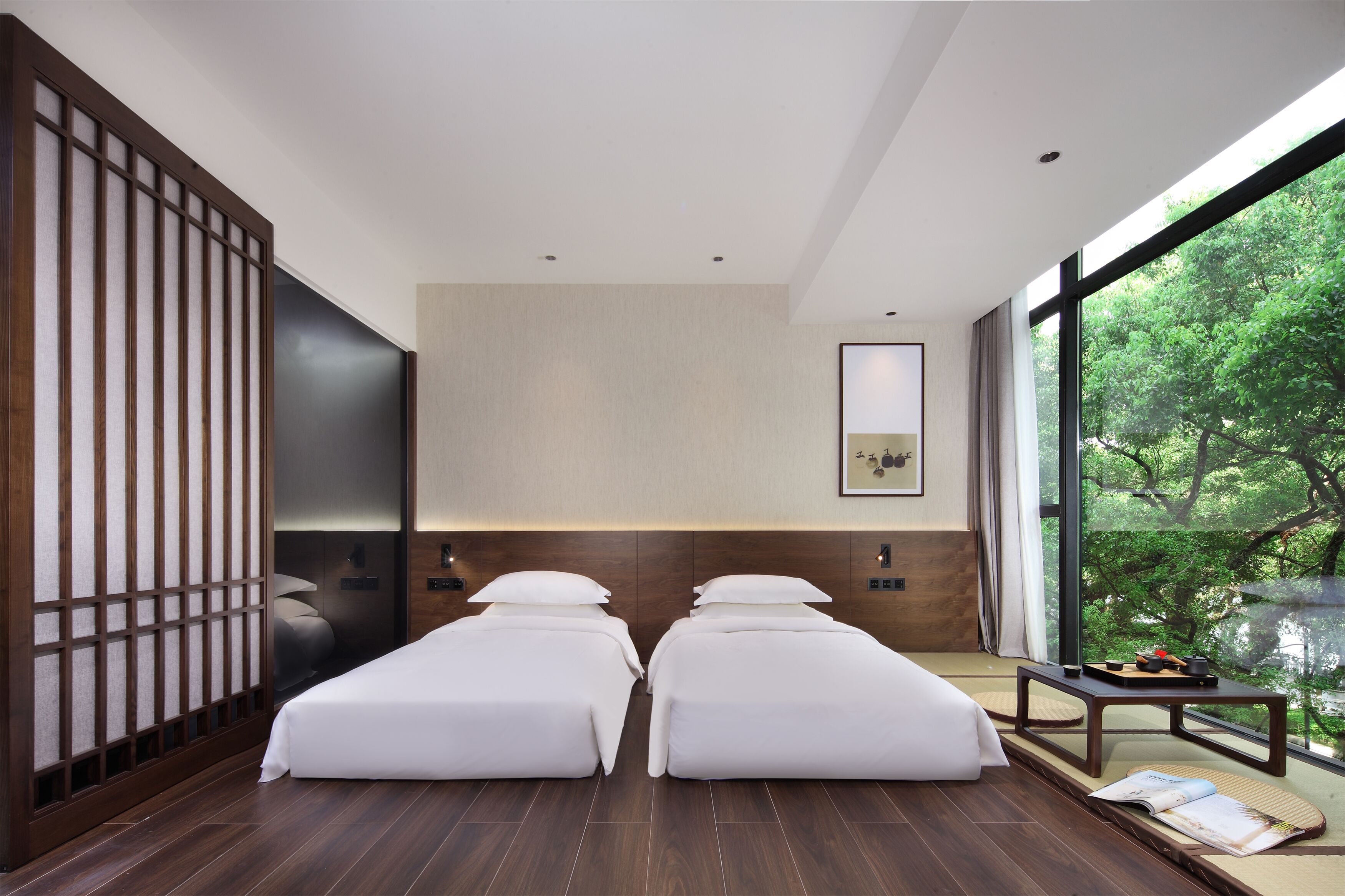 Une chambre d’hôtel moderne avec deux lits, une grande fenêtre donnant sur la verdure et une porte coulissante de style traditionnel.