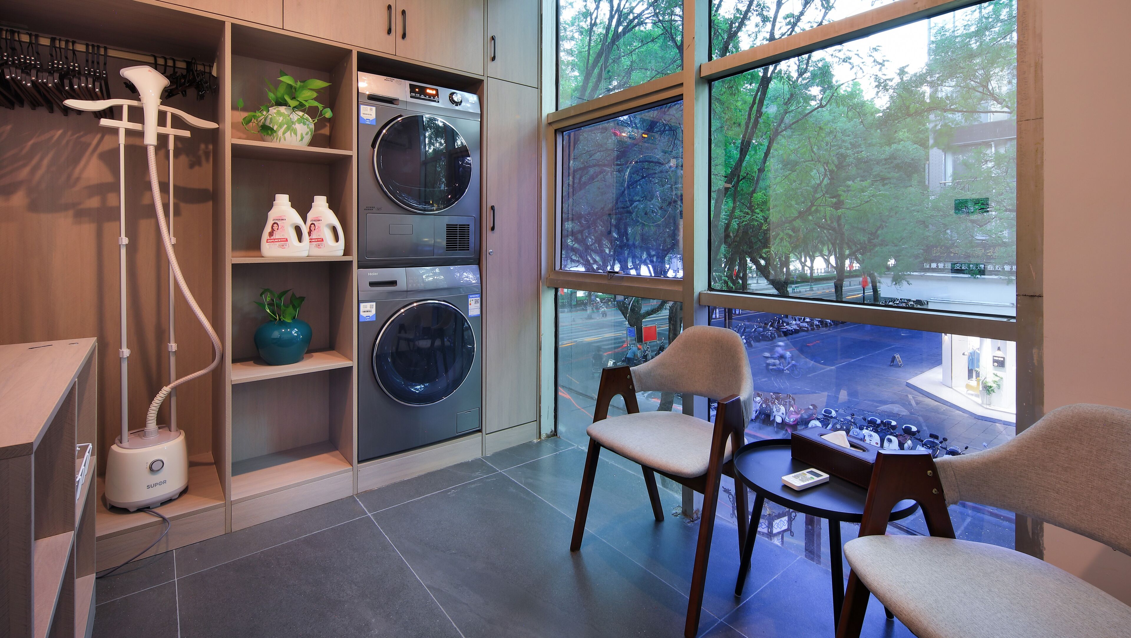 A modern laundry room with a large window, a washing machine, a dryer, and a chair.