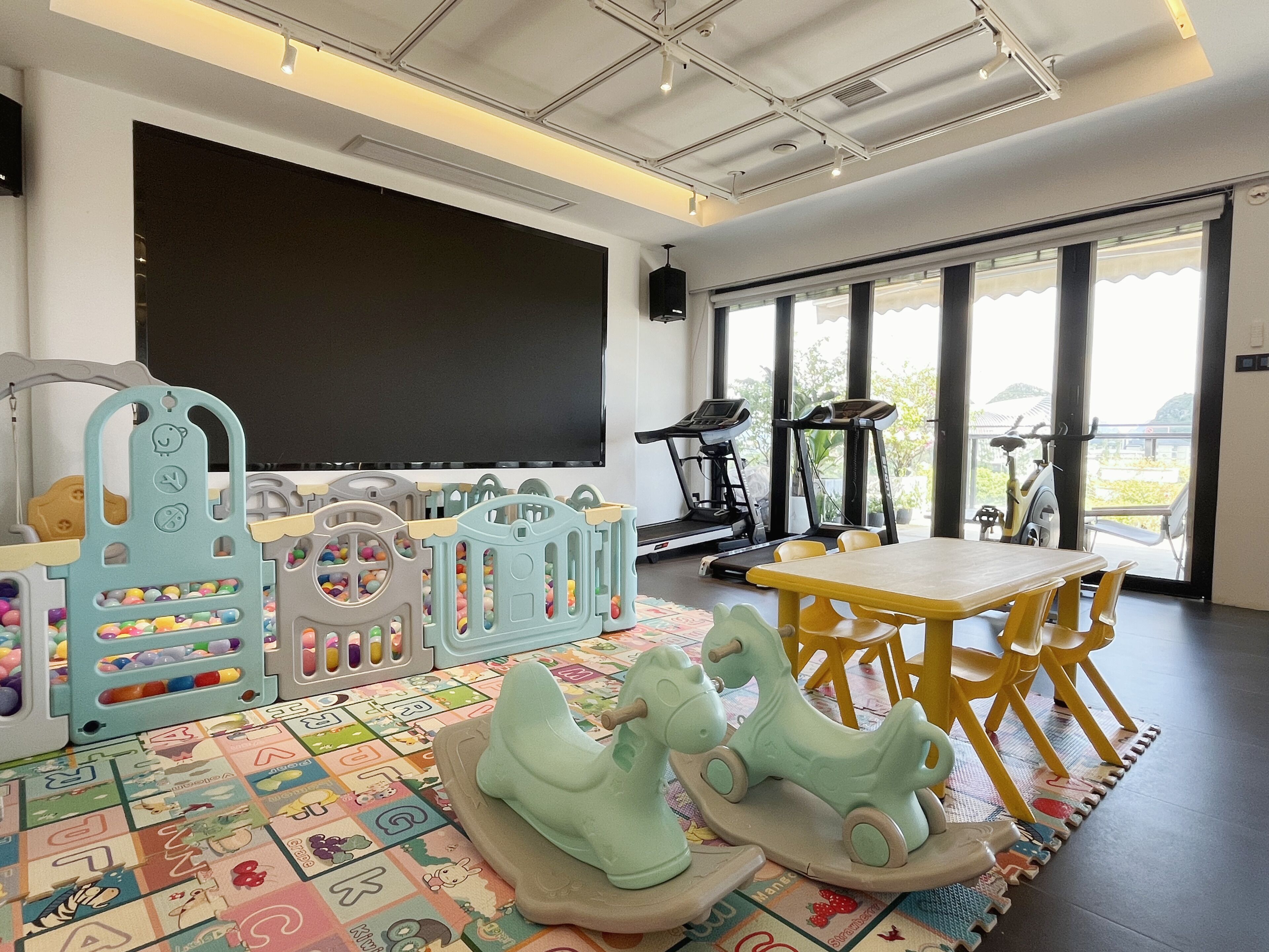 Espaço infantil com uma televisão grande, bicicletas ergométricas e uma mesa com cadeiras.