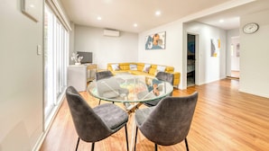 Un salon moderne avec une table à manger au plateau en verre, des chaises à revêtement gris, un canapé jaune et un plancher en bois.