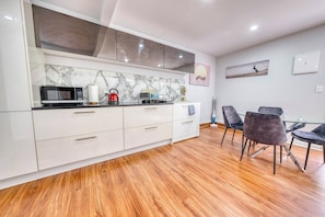 Una cocina moderna con microondas, hervidor y comedor con sillas.