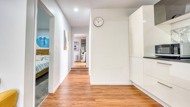 Un couloir étroit avec un plancher en bois, un lit avec une literie à rayures, une armoire blanche et un four à micro-ondes sur la droite.