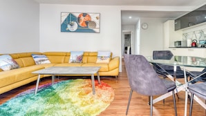Un salon moderne avec un canapé jaune, une table à manger en verre et un tapis coloré.