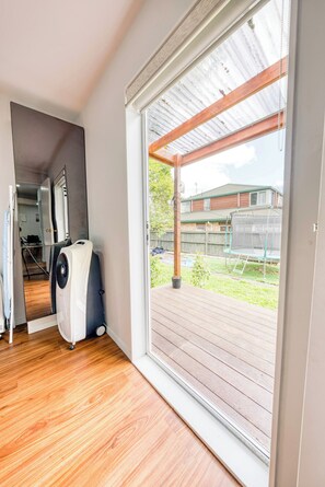 A room with a sliding glass door to a deck, a white fan, and a wooden floor. - Auckland's Urban Escape - Central, Connected & Comfortable (Auckland)
