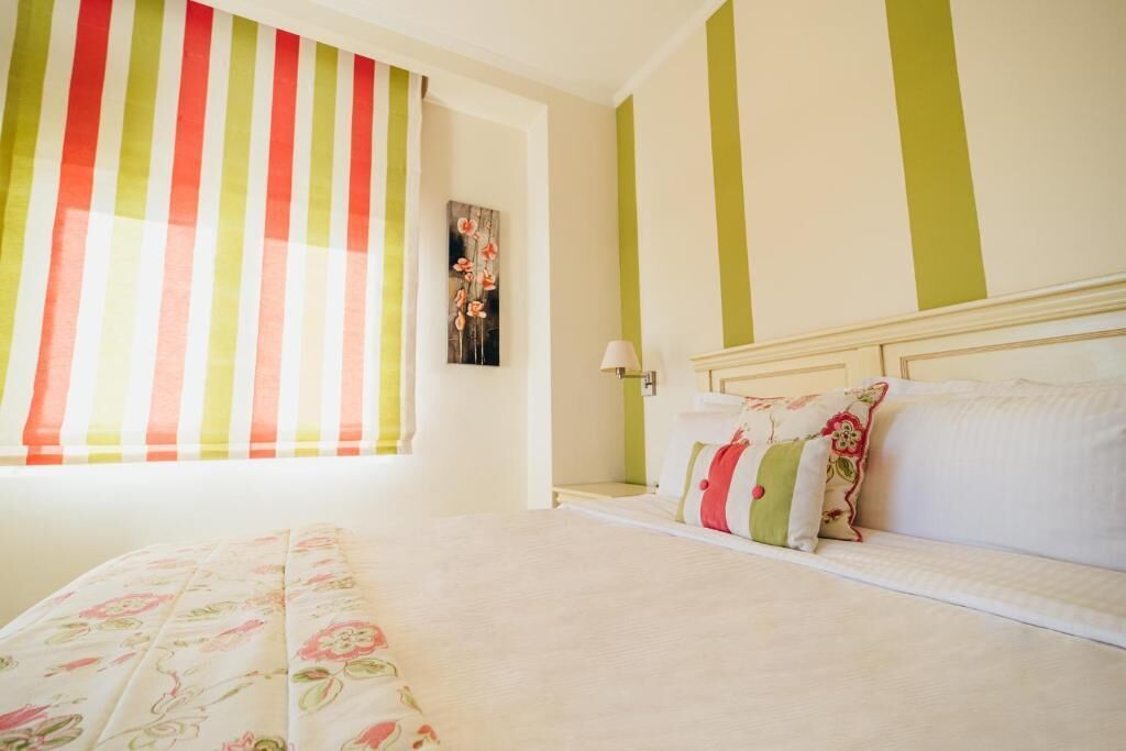 A bedroom with a bed, pillows, a nightstand, a lamp, and a window with striped curtains.