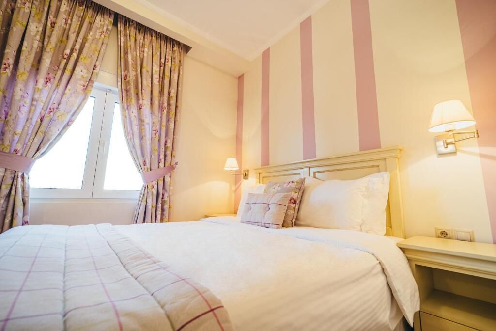 Quarto de hotel com cama, cortinas, mesa de cabeceira e luminárias na parede.