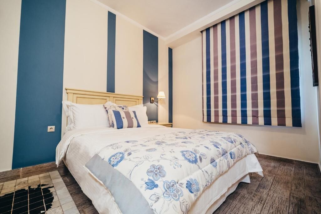 Un dormitorio con cama, mesita de noche, lámpara y ventana con cortinas a rayas.