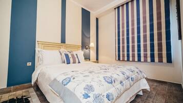Un dormitorio con cama, mesita de noche, lámpara y ventana con cortinas a rayas.