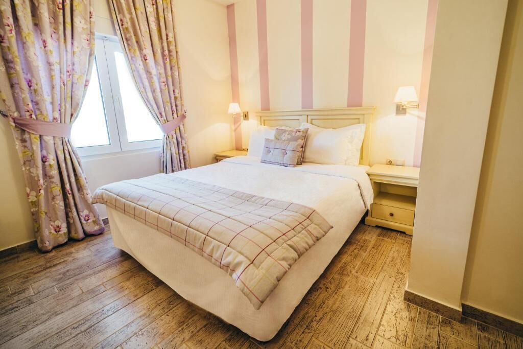 Un dormitorio ordenado con una cama grande, dos mesitas de noche y una ventana con cortinas.