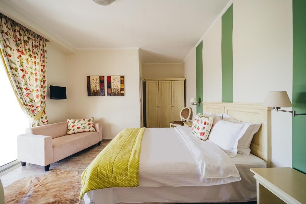 A hotel room with a bed, a sofa, a television, and artwork on the wall.