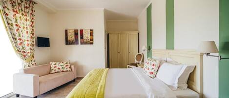A hotel room with a bed, a sofa, a television, and artwork on the wall.