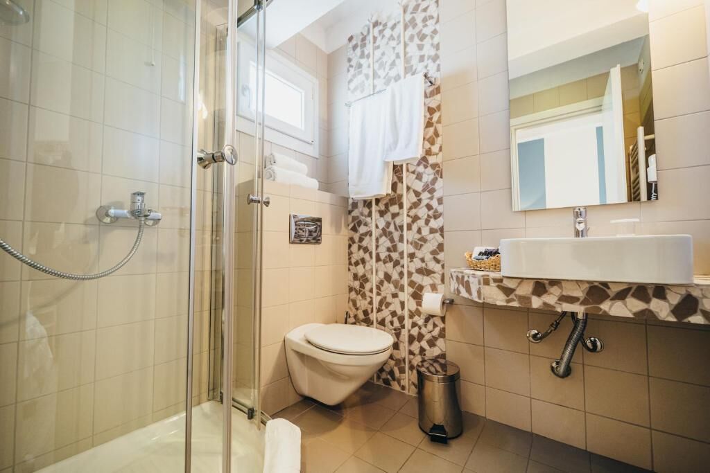 Un baño con ducha de vidrio, inodoro, lavamanos con espejo y azulejos estampados.