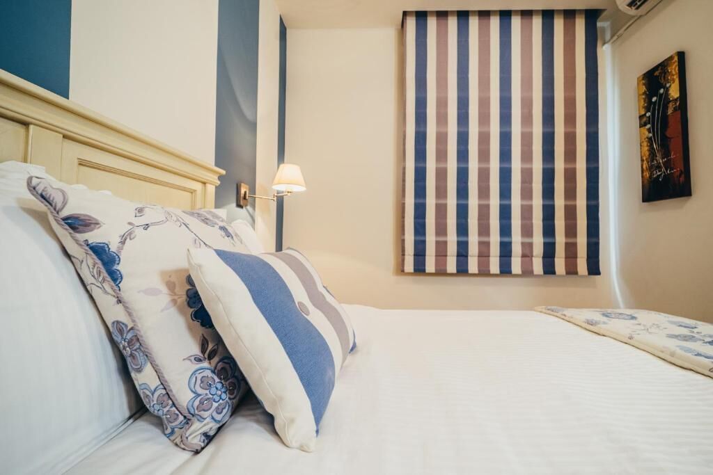 A neatly made bed with patterned pillows, a striped curtain, and a wall-mounted lamp.