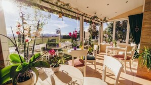 Une terrasse ensoleillée, avec des tables et des chaises rondes, entourée de plantes et de fleurs en pot.