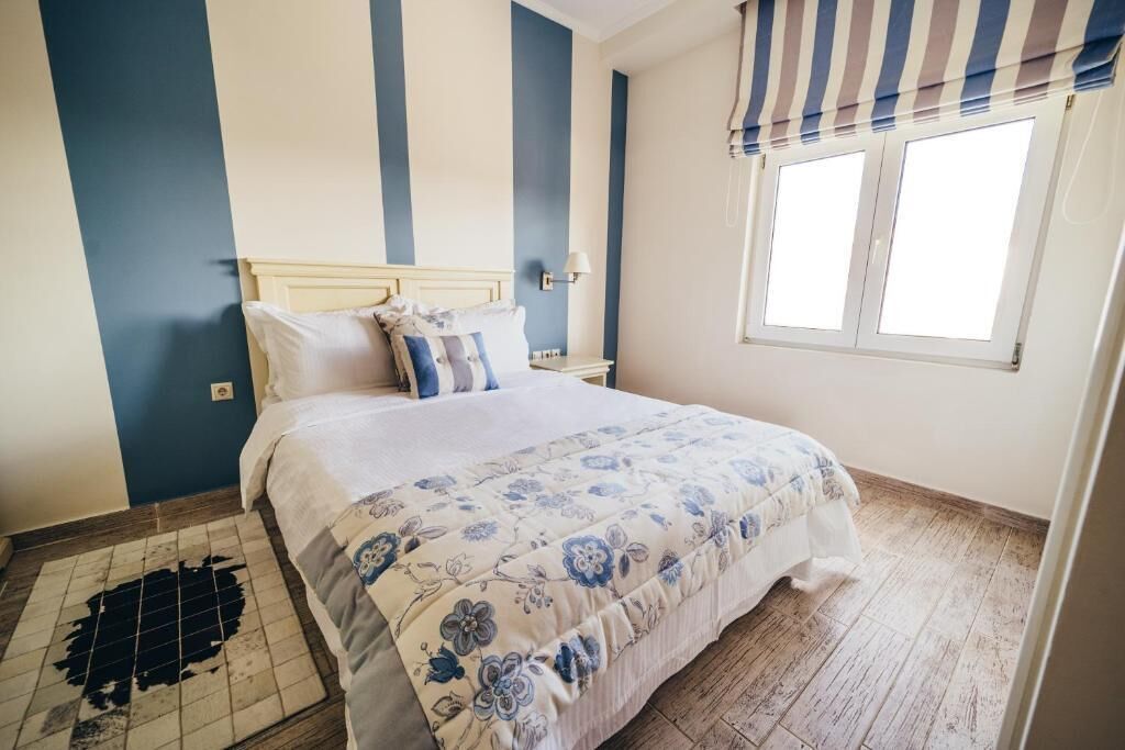 Une chambre à coucher avec un lit, une table de chevet, une lampe et une fenêtre avec un rideau à rayures.