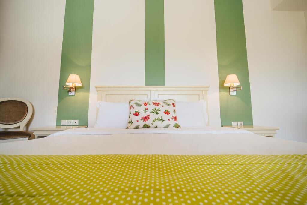 A hotel room with a large bed, green walls, and two bedside lamps.