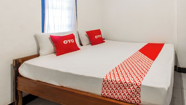 A bed with white bedding and red pillows, a wooden headboard, and a window with blue curtains. - Hotel O Kawi Homestay (Praya Barat Daya)