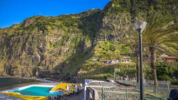 A coastal swimming pool with a view of a mountainous landscape.