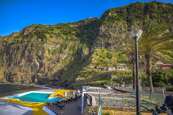 A coastal swimming pool with a view of a mountainous landscape.