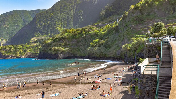 A beach with people sunbathing and swimming, surrounded by lush green hills and a clear blue sea. - Paradise town with ocean pool, mountains, waterfalls, surfing, shops and bars.  (Ponta Delgada svc 2879-S Vicente)