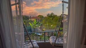A balcony with two cushioned swing chairs, a view of a garden, and a house in the background. - Paradise town with ocean pool, mountains, waterfalls, surfing, shops and bars.  (Ponta Delgada svc 2879-S Vicente)