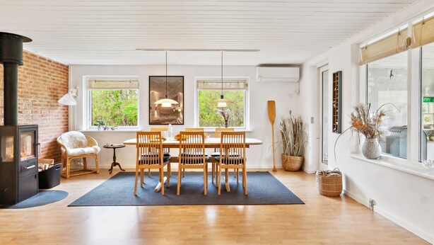 A cozy room with a dining table, chairs, a fireplace, and large windows offering a view of greenery.