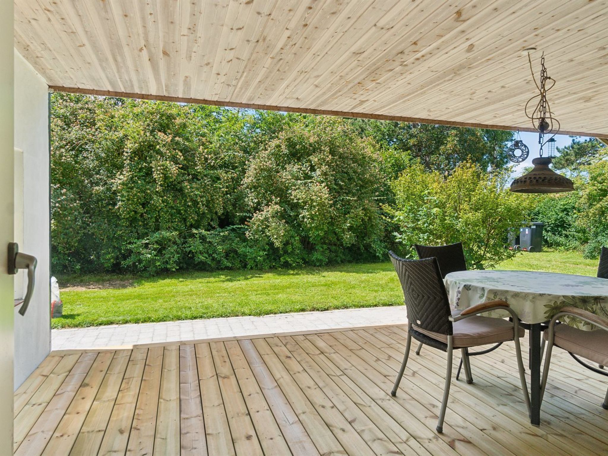 Une terrasse en bois aménagée à l’extérieur, avec une table et des chaises, entourée d’une végétation luxuriante.