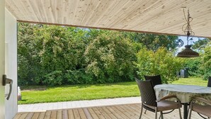 An outdoor wooden deck with a table and chairs, surrounded by lush greenery.