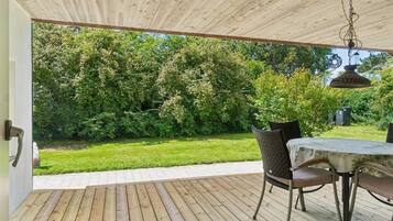 Une terrasse en bois aménagée à l’extérieur, avec une table et des chaises, entourée d’une végétation luxuriante.