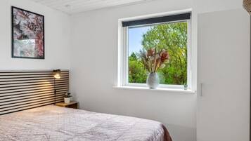 Une chambre à coucher avec un lit, une fenêtre donnant sur un paysage verdoyant, un tableau accroché au mur et une lampe de chevet.