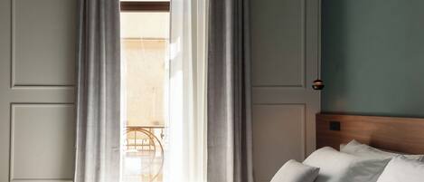 Ett hotellrum med en säng, gardiner, utsikt över balkongen och en hänglampa.
