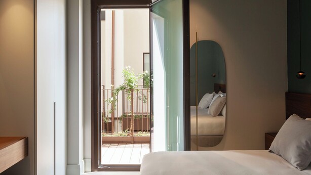 A modern bedroom with a bed, a large mirror, and a sliding glass door leading to a balcony with plants. - Palazzo Giusti Lecce - Exclusive Boutique Hotel (Lecce)