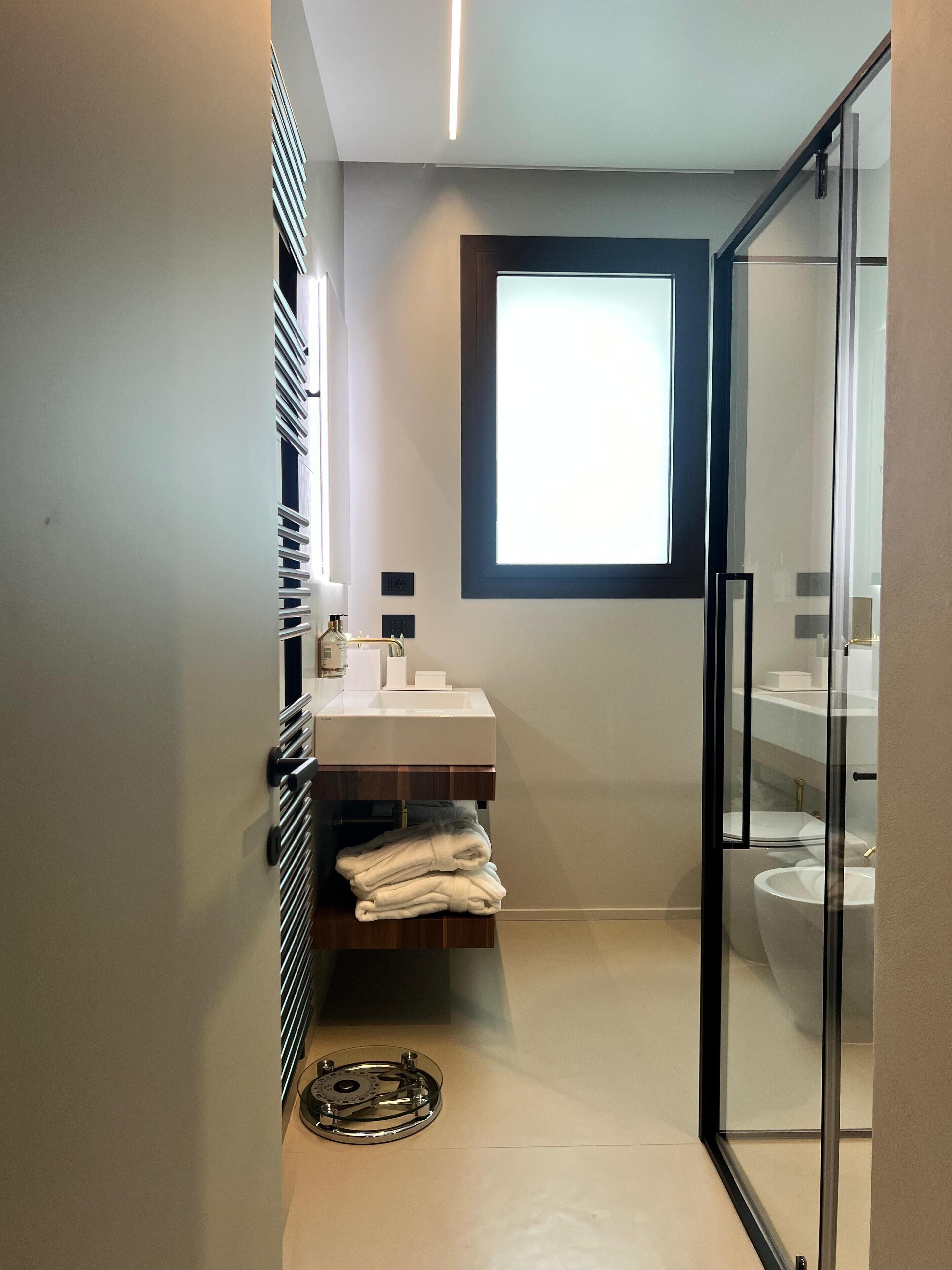 A modern bathroom with a glass shower enclosure, a white sink, and a window providing natural light.
