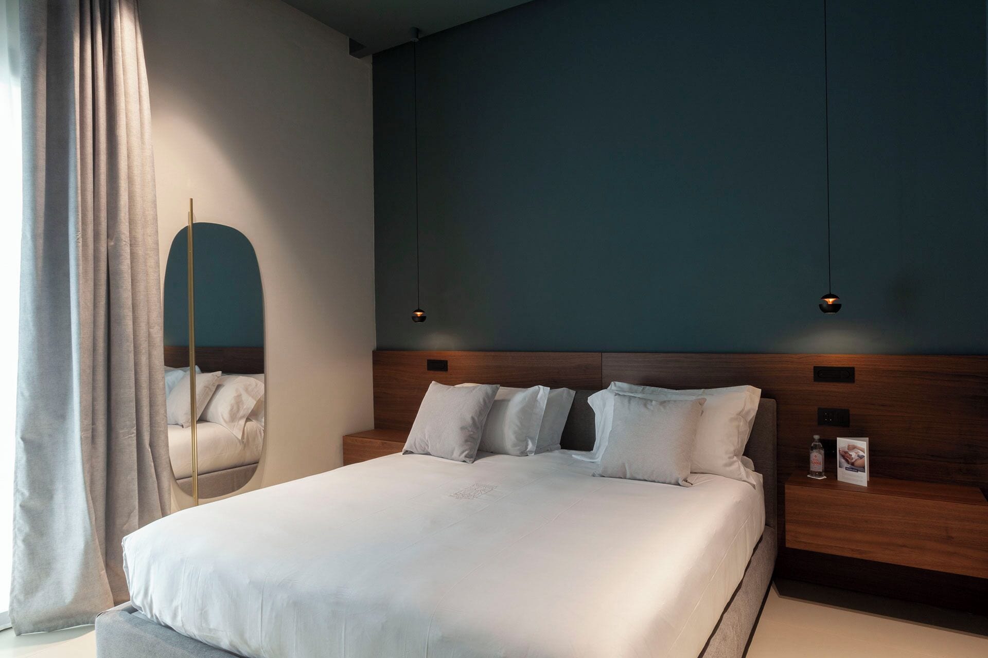 Una camera d'albergo moderna con un letto grande, una testiera in legno e uno specchio.